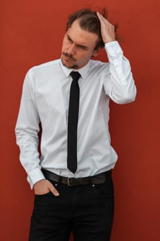 Portrait of startup businessman in a white shirt with a black tie standing in front of the red wall outside. High-quality photo