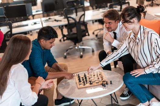 Multiethnic group of businesspeople playing chess while having a break in relaxation area at modern startup office. High-quality photo