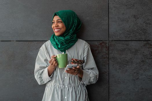African Muslim businesswoman with green hijab using a smartphone during a coffee break from work outside. High-quality photo