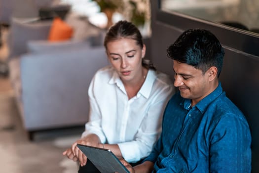 Multiethnic business people man with a female colleague working together on tablet computer in relaxation area of modern startup office. High-quality photo