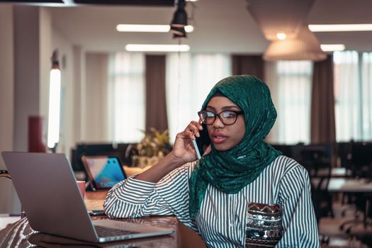 Smiling young woman talk on smartphone work on laptop look in distance thinking. Happy African American customer client using modern gadgets cellphone and computer at the home office. High-quality photo