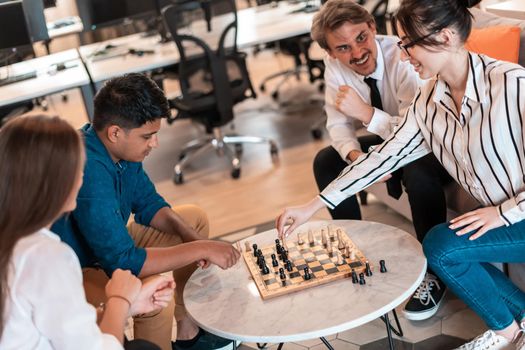 Multiethnic group of businesspeople playing chess while having a break in relaxation area at modern startup office. High-quality photo