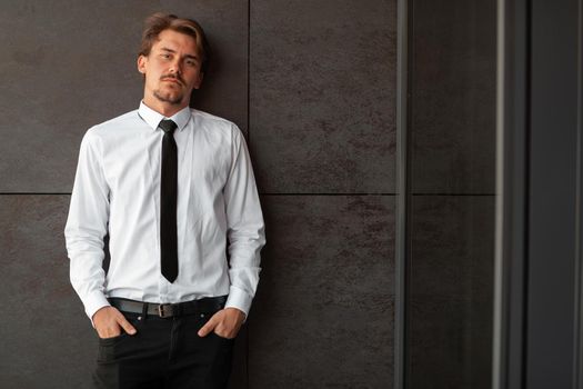 Portrait of startup businessman in a white shirt with a black tie standing in front of the gray wall outside. High-quality photo