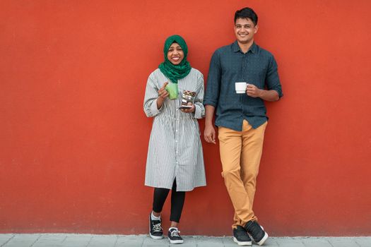 Multiethnic group of casual businesspeople using smartphones during a coffee break from work in front of the red wall outside. High-quality photo