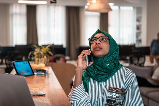 Smiling young woman talk on smartphone work on laptop look in distance thinking. Happy African American customer client using modern gadgets cellphone and computer at the home office. High-quality photo