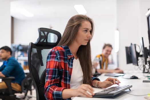 Casual businesswoman working on a desktop computer in modern open plan startup office interior. Selective focus. High-quality photo