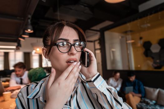 Businesswoman with glasses using a smartphone at modern startup open plan office interior. Selective focus. High-quality photo