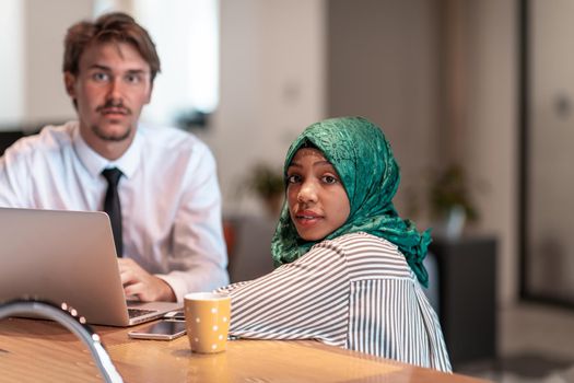 International multicultural business team.Man and Muslim woman with hijab working together using smartphone and laptop location area at modern open plan startup office puter in real. High-quality photo