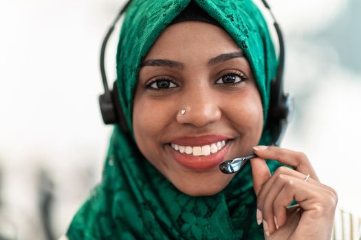 Afro Muslim female with green hijab scarf customer representative businesswoman with phone headset helping and supporting online with the customer in a modern call center. High-quality photo