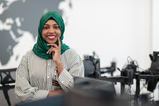 Portrait of Muslim black female software developer with green hijab standing at modern open plan startup office. Selective focus. High-quality photo