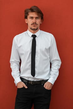 Portrait of startup businessman in a white shirt with a black tie standing in front of the red wall outside. High-quality photo