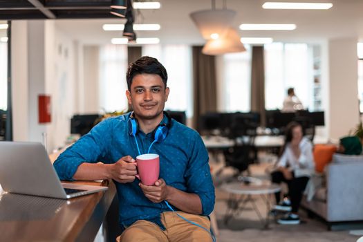 Casual businessman taking a break from the work using a laptop while drinking tea in relaxation area of modern open plan startup office. High-quality photo