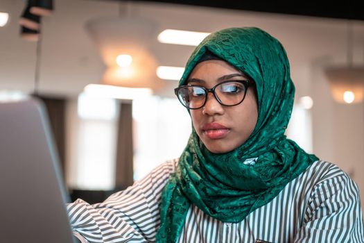 Businesswoman wearing a green hijab using laptop in relaxation area at modern open plan startup office. Selective focus. High-quality photo