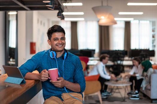 Casual businessman taking a break from the work using a laptop while drinking tea in relaxation area of modern open plan startup office. High-quality photo