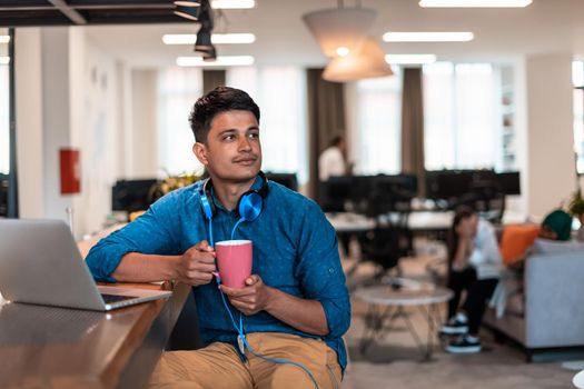 Casual businessman taking a break from the work using a laptop while drinking tea in relaxation area of modern open plan startup office. High-quality photo