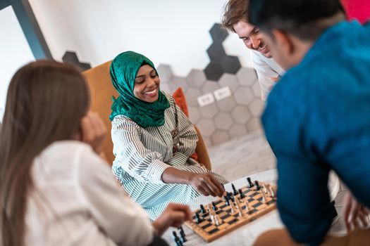 Multiethnic group of businesspeople playing chess while having a break in relaxation area at modern startup office. Selective focus. High-quality photo