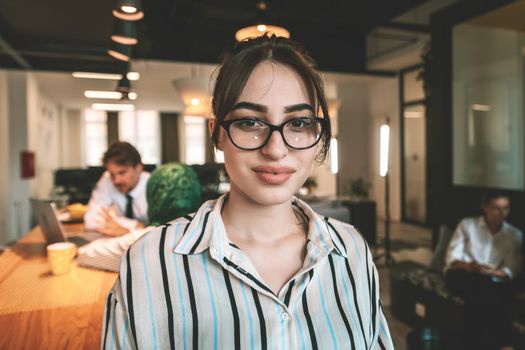 Portrait of businesswoman in casual clothes with glasses at modern startup open plan office interior. Selective focus. High-quality photo