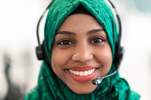 Afro Muslim female with green hijab scarf customer representative businesswoman with phone headset helping and supporting online with the customer in a modern call center. High-quality photo