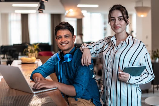 Multiethnic business people man with a female colleague working together on tablet and laptop computer in relaxation area of modern startup office. High-quality photo