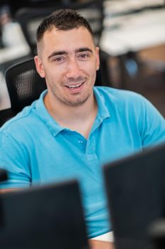 Casual businessman working on a desktop computer in modern open plan startup office interior. Selective focus. High-quality photo