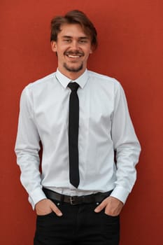 Portrait of startup businessman in a white shirt with a black tie standing in front of the red wall outside. High-quality photo