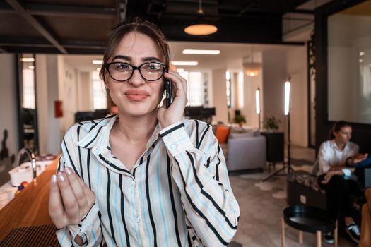 Businesswoman with glasses using a smartphone at modern startup open plan office interior. Selective focus. High-quality photo