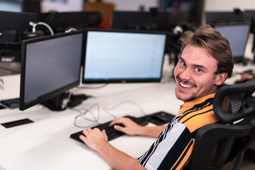 Casual man working on a desktop computer in modern open plan startup office interior. Selective focus. High-quality photo