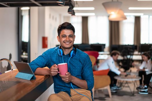 Casual businessman taking a break from the work using a laptop while drinking tea in relaxation area of modern open plan startup office. High-quality photo