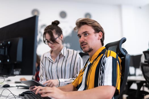 Business couple working together on a project using tablet and desktop computer at modern open plan startup office. Selective focus. High-quality photo