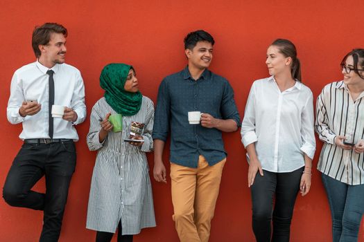 Multiethnic group of casual businesspeople using smartphones during a coffee break from work in front of the red wall outside. High-quality photo