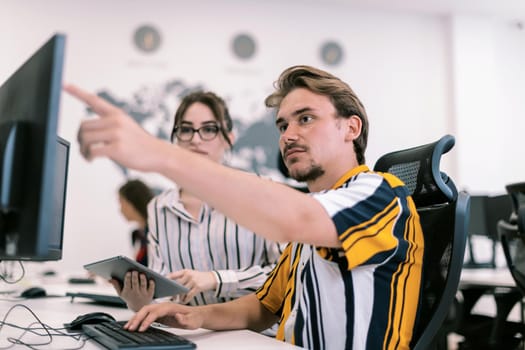 Business couple working together on a project using tablet and desktop computer at modern open plan startup office. Selective focus. High-quality photo