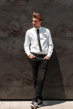 Portrait of startup businessman in a white shirt with a black tie standing in front of the gray wall outside. High-quality photo