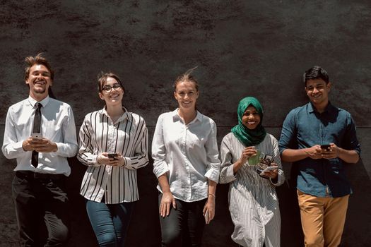 Multiethnic group of casual businesspeople using a smartphone during a coffee break from work in front of the black wall outside. High-quality photo