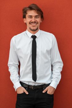 Portrait of startup businessman in a white shirt with a black tie standing in front of the red wall outside. High-quality photo