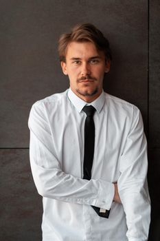 Portrait of startup businessman in a white shirt with a black tie standing in front of the gray wall outside. High-quality photo