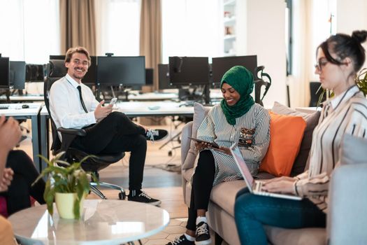 Multiethnic startup business team having brainstorming in relaxation area of modern office interior working on laptop and tablet computer. High-quality photo