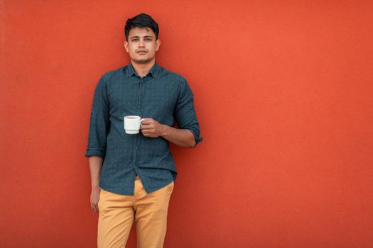 Startup business portrait of casual businessman with a blue shirt and coffee standing in front of a red wall. High-quality photo