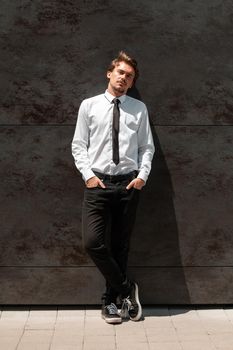 Portrait of startup businessman in a white shirt with a black tie standing in front of the gray wall outside. High-quality photo