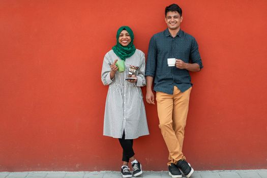 Multiethnic group of casual businesspeople using smartphones during a coffee break from work in front of the red wall outside. High-quality photo