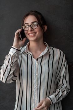 Startup businesswoman in shirt with a glasses using smartphone while standing in front of gray wall during a break from work outside. High-quality photo