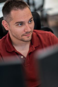 Casual businessman working on a desktop computer in modern open plan startup office interior. Selective focus. High-quality photo