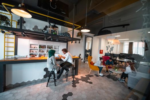 Group of casual multiethnic businesspeople taking a break from the work doing different things while enjoying free time in relaxation area at modern open plan startup office. High-quality photo