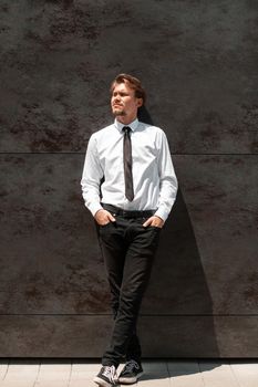 Portrait of startup businessman in a white shirt with a black tie standing in front of the gray wall outside. High-quality photo