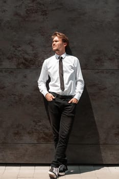 Portrait of startup businessman in a white shirt with a black tie standing in front of the gray wall outside. High-quality photo