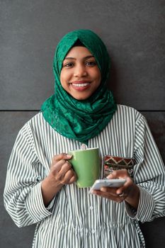 African Muslim businesswoman with green hijab using a smartphone during a coffee break from work outside. High-quality photo