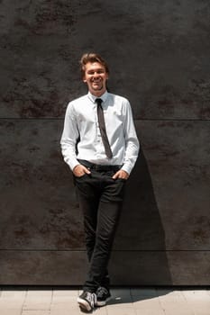 Portrait of startup businessman in a white shirt with a black tie standing in front of the gray wall outside. High-quality photo