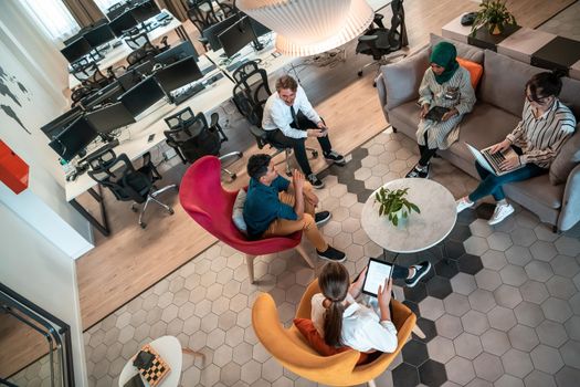 Top view photo of Multiethnic startup business team having brainstorming in relaxation area of modern office interior working on laptop and tablet computer. High-quality photo