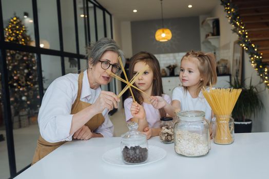 Grandmother and granddaughter are cooking on kitchen. Playing with pasta