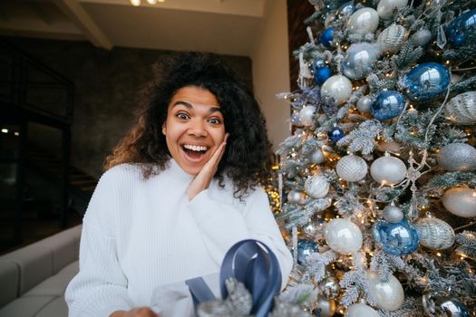Woman gives a gift to his friend in the camera. Portrait of a young woman of Afro appearance ethnic, black curly hair brunette.