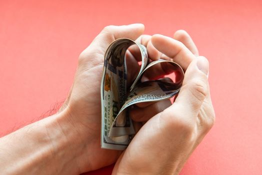 several 100 dollar bills folded in the shape of a heart in male hands. love of money, greed, business, wealth.